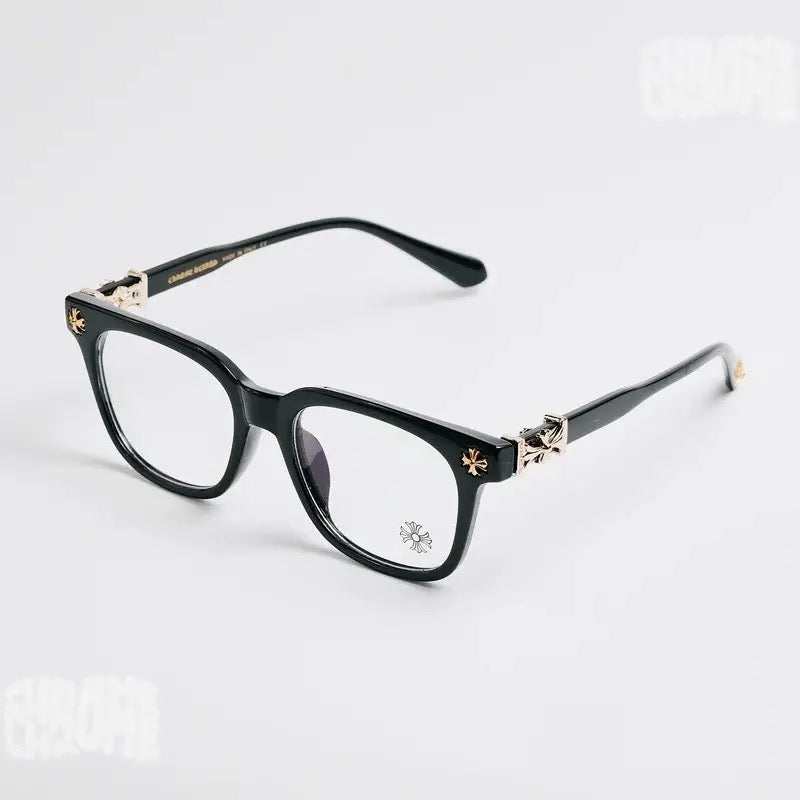 Black acetate square eyeglasses with gold-tone decorative hardware and clear lenses, photographed on a clean light gray background.
