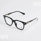 Black acetate square eyeglasses with gold-tone decorative hardware and clear lenses, photographed on a clean light gray background.